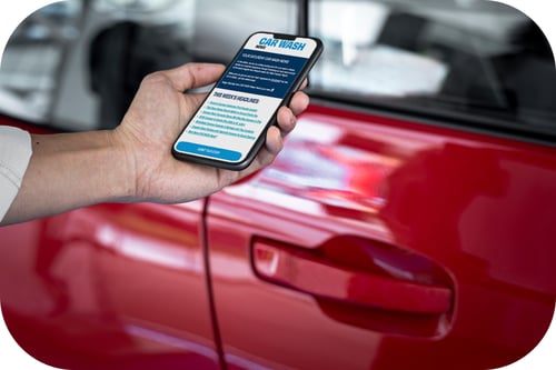 A man reading CAR WASH News on his phone next to his car